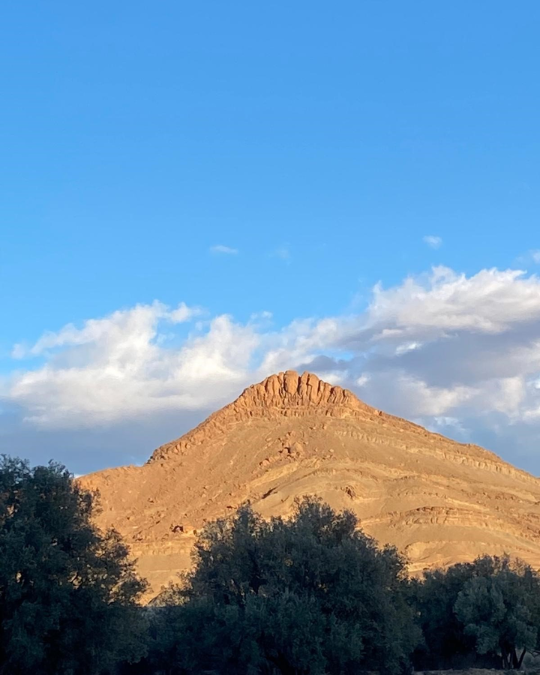 Montagne ocre baignée de lumière dorée sous un ciel bleu au Maroc.