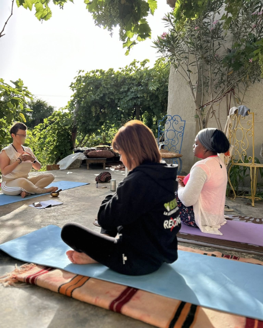 Femmes assises en cercle sous une pergola végétalisée pratiquant un temps de régulation en plein air.