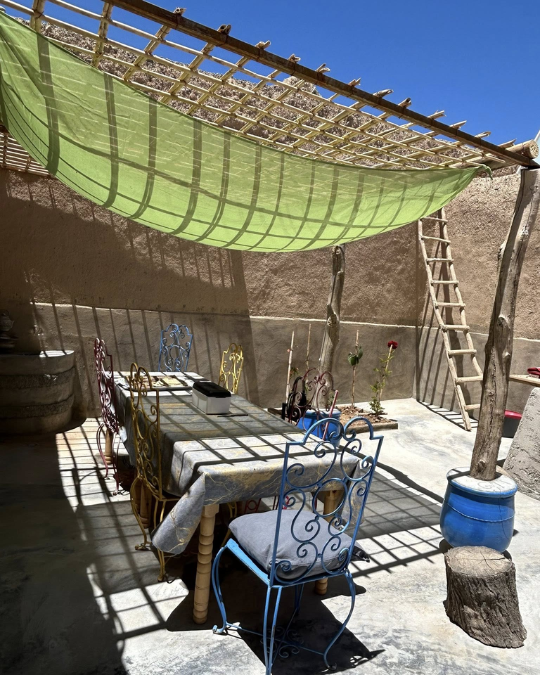Table extérieure sous une toile d’ombrage avec chaises colorées dans le patio du gîte.